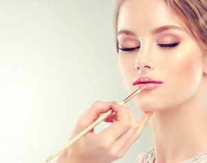 Hand of make-up master, painting lips of young beautiful model. Make-up in progress.