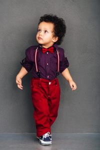 Little African baby boy looking away while walking against grey background